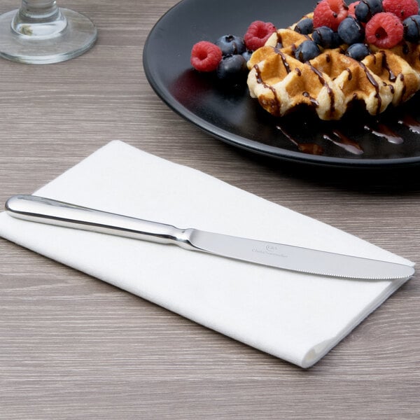 A silver Chef & Sommelier stainless steel dessert knife on a white surface next to a plate of waffles and berries.
