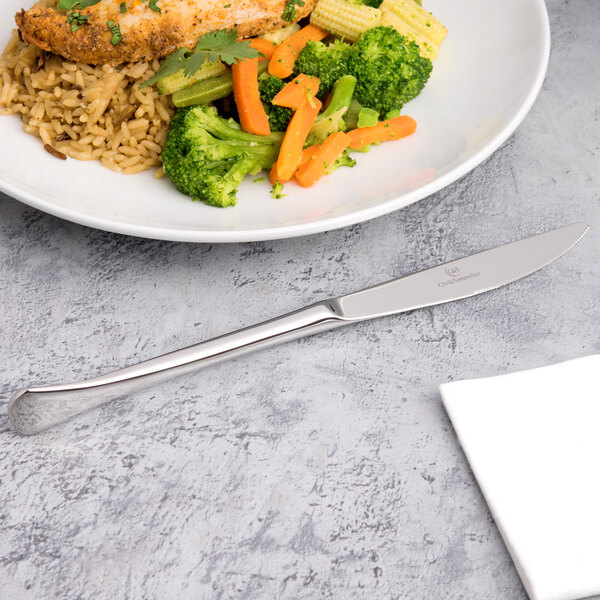 A plate of food with rice, broccoli, and carrots next to a silver Chef & Sommelier dinner knife.