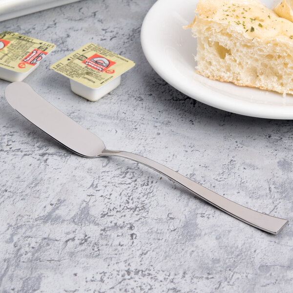 A butter spreader on a table with a plate of food and a piece of bread.