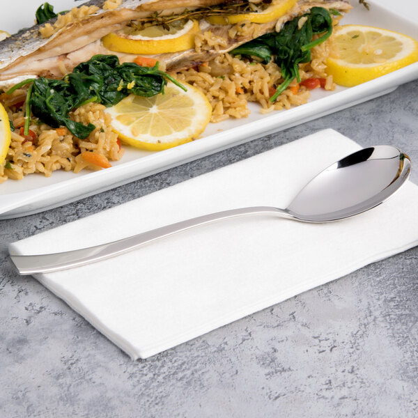 An Arcoroc stainless steel dinner spoon on a white surface in a seafood restaurant near a plate of food.
