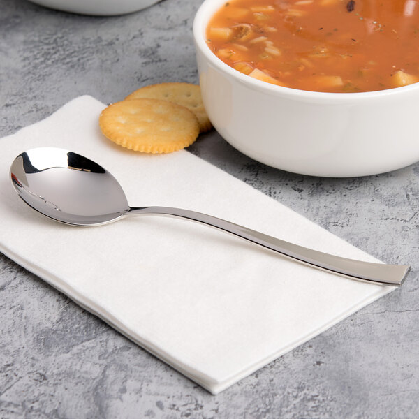 A bowl of soup with a spoon and crackers on a white napkin.