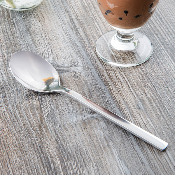 A Libbey stainless steel dessert spoon on a table with a glass of coffee.