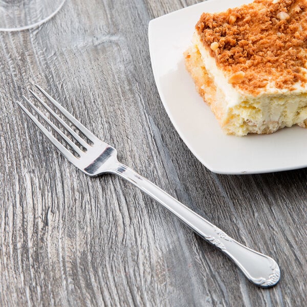 A Libbey stainless steel utility fork on a plate with a piece of cake.
