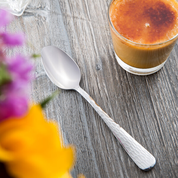 A Libbey stainless steel teaspoon on a table next to a glass of orange juice.