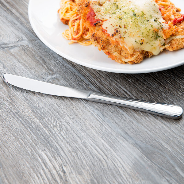 A Libbey stainless steel knife with a fluted blade on a table with a plate of spaghetti.