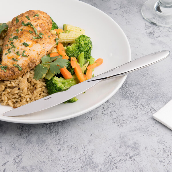 A Arcoroc stainless steel dinner knife on a plate of chicken, rice, and vegetables.