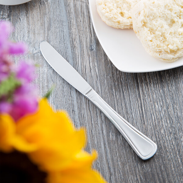 A Libbey stainless steel bread and butter knife on a table next to a plate of biscuits.
