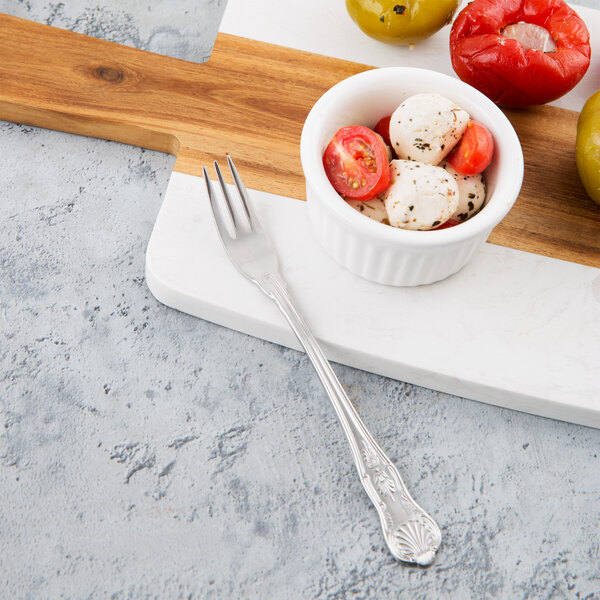 A bowl of mozzarella, tomatoes, and peppers with a Libbey Kings stainless steel cocktail fork on a white cutting board.