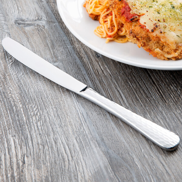 A plate of spaghetti with meat sauce and a Libbey Aspire dinner knife on a table.