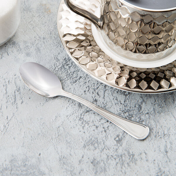 A Libbey stainless steel demitasse spoon in a silver cup on a saucer.