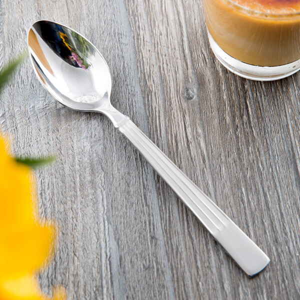 A Libbey stainless steel teaspoon on a table next to a cup of coffee.