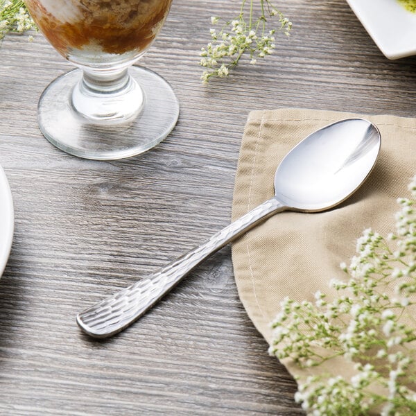 A Libbey medium weight stainless steel dessert spoon on a napkin next to a glass of dessert.
