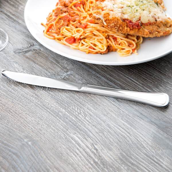 A Libbey stainless steel dinner knife on a table next to a plate of spaghetti and meat.