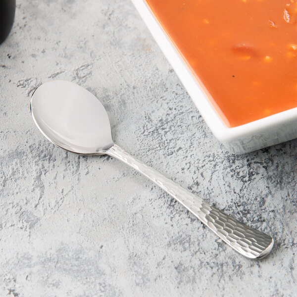 A Libbey medium weight stainless steel bouillon spoon next to a bowl of soup.