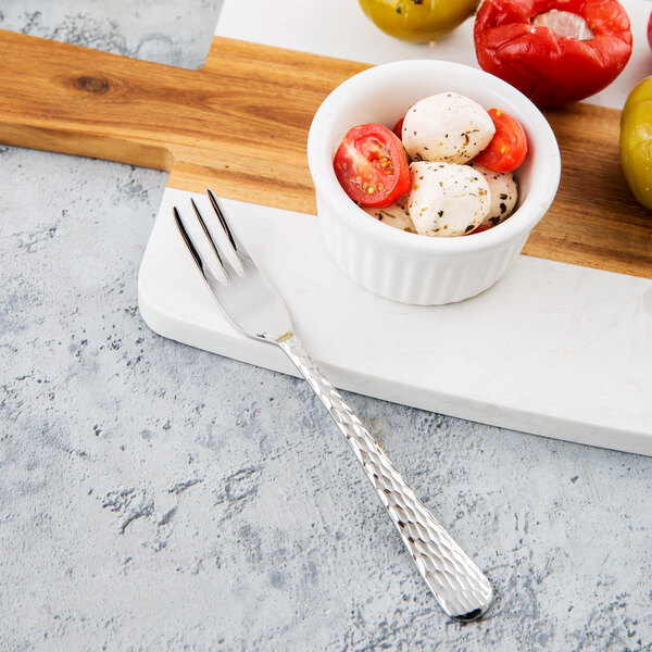 A bowl of tomatoes and mozzarella cheese with a Libbey stainless steel cocktail fork on a cutting board.