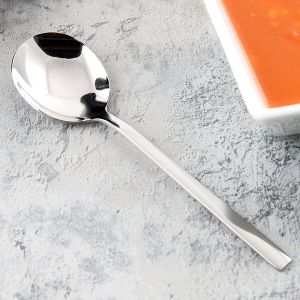 A Libbey stainless steel bouillon spoon in a bowl of soup on a table.
