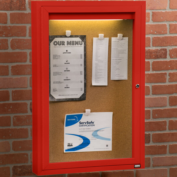 An Aarco red indoor bulletin board cabinet with papers inside.