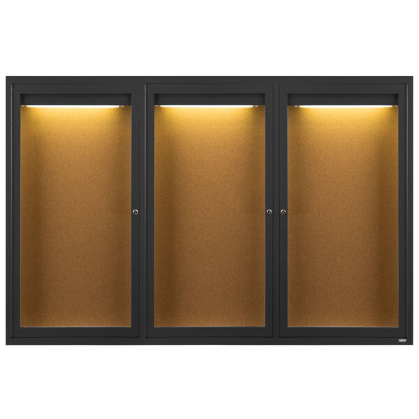 A black Aarco bulletin board cabinet with 3 glass doors and lights on a brown surface.