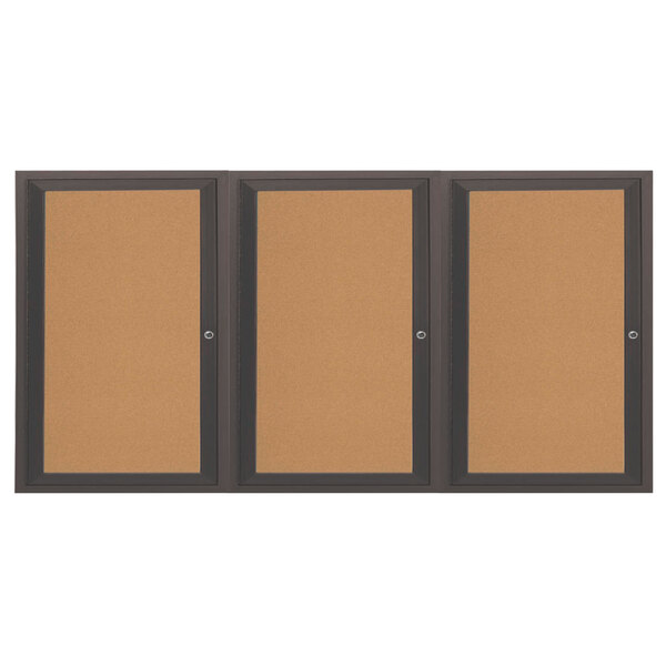 An Aarco bronze anodized indoor bulletin board cabinet with three black framed bulletin boards behind three doors.