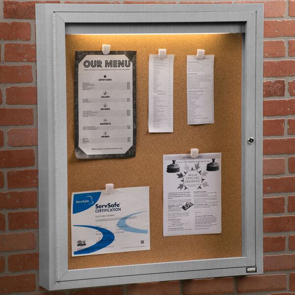 An Aarco lighted indoor bulletin board cabinet with cork board inside.
