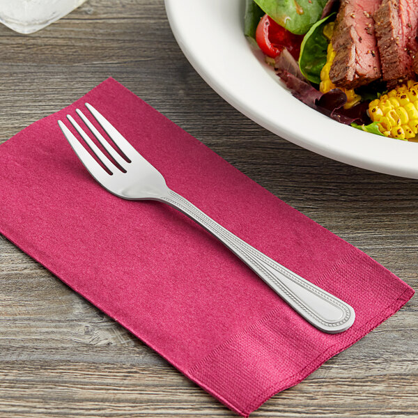 A Choice Milton stainless steel salad fork on a napkin next to a plate of salad