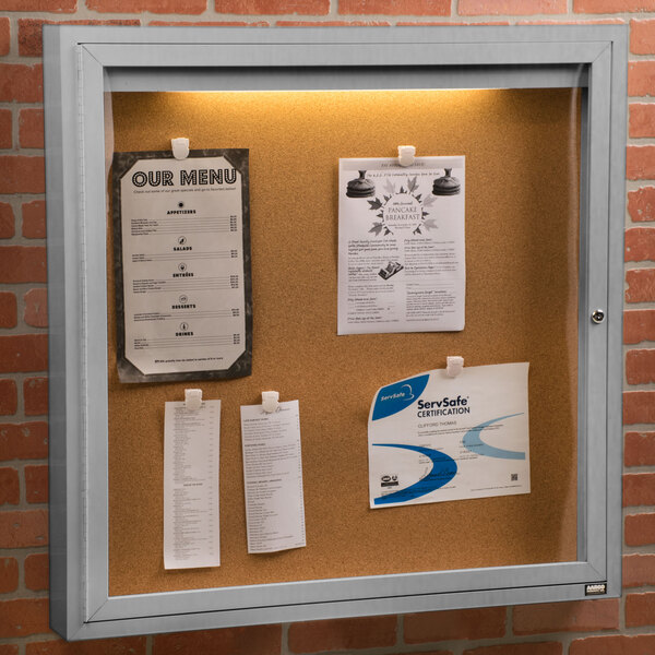 An Aarco satin anodized finish bulletin board cabinet with a lighted sign on it.