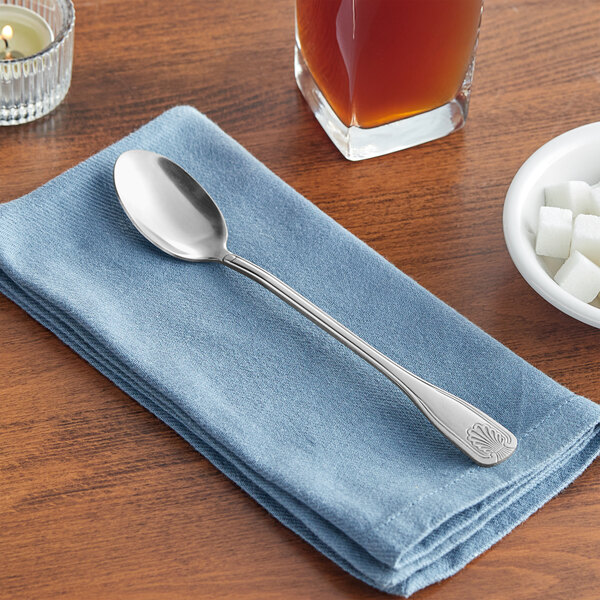 An Acopa stainless steel iced tea spoon on a napkin next to a glass of liquid and a candle.