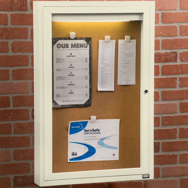An ivory Aarco enclosed bulletin board with paper pinned to it.