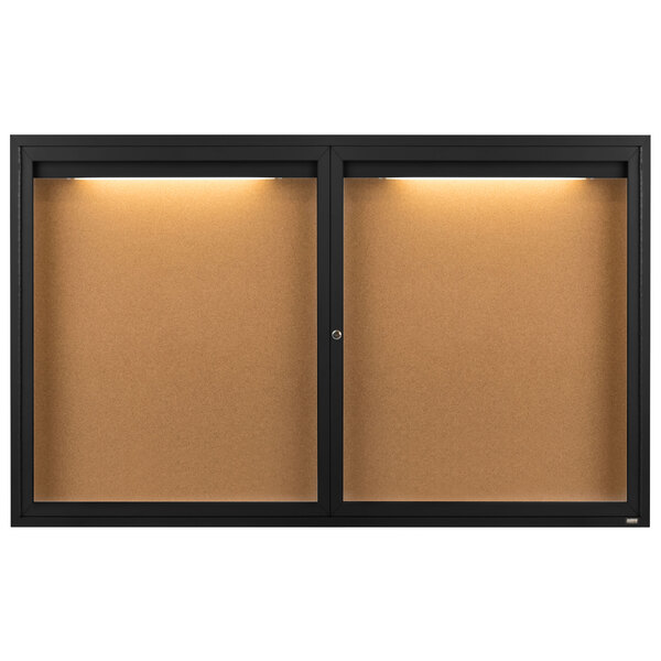 An Aarco black powder coated enclosed bulletin board with lights on a wall.