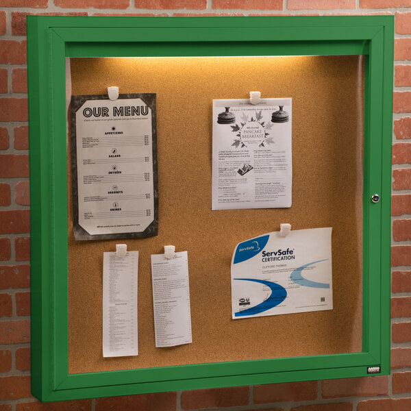 An Aarco green enclosed bulletin board cabinet with 1 door and a green light inside.