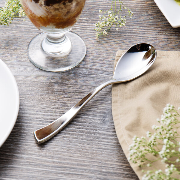 A Chef & Sommelier stainless steel dessert spoon on a napkin next to a glass of ice cream.