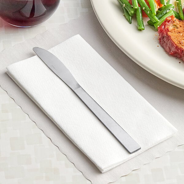 A Choice Windsor stainless steel dinner knife on a napkin next to a plate of food.