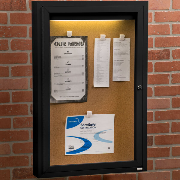 An Aarco black indoor lighted bulletin board cabinet with paper on it.