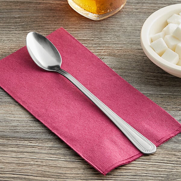 A Choice Milton stainless steel iced tea spoon on a napkin next to a bowl of sugar cubes.