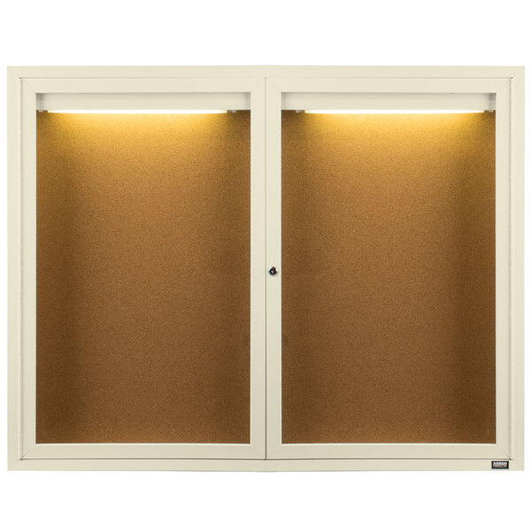 A white Aarco bulletin board cabinet with two doors and lights on it.