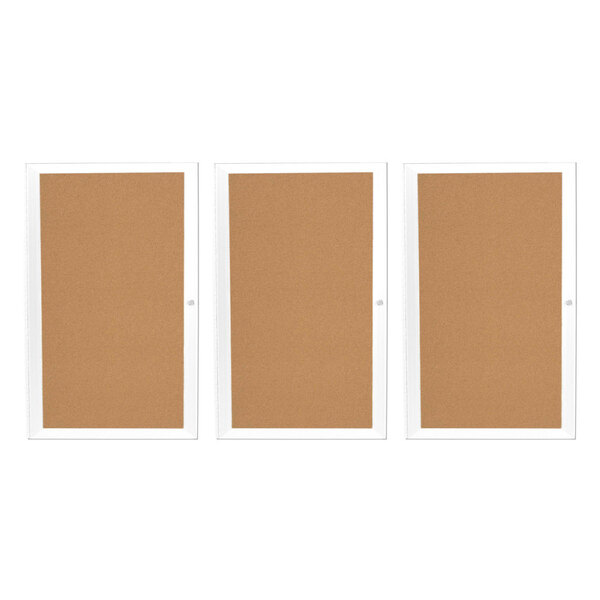 An Aarco white indoor bulletin board cabinet with three brown cork boards.