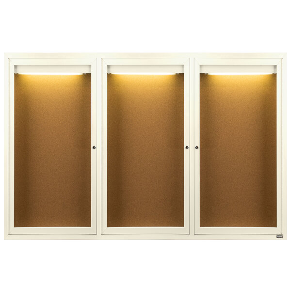 Three white Aarco bulletin board cabinets with glass doors on a cork board with lights.