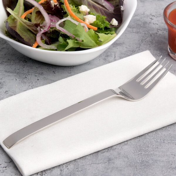 An Arcoroc stainless steel salad fork on a napkin next to a bowl of salad.