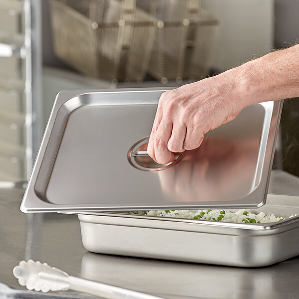 A hand opening a stainless steel steam table pan cover over food.