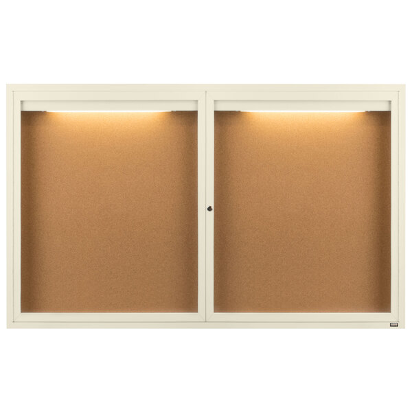 A white framed Aarco bulletin board cabinet with two enclosed glass doors and lights.
