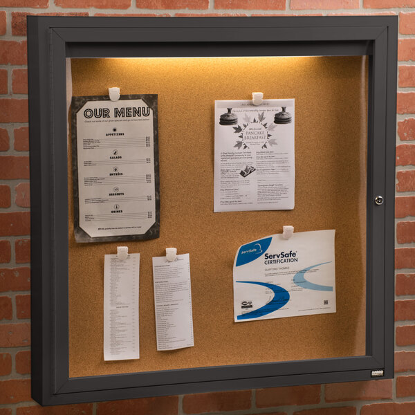 An Aarco bronze indoor lighted cork bulletin board with papers attached to it.