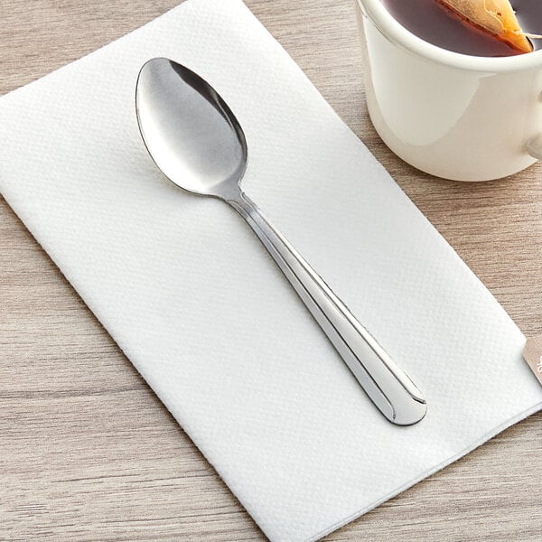 A Choice Dominion stainless steel teaspoon on a napkin next to a cup of tea.
