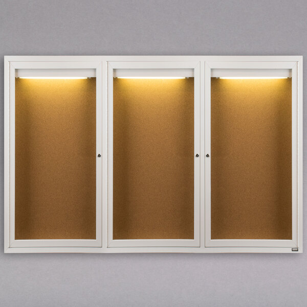 An Aarco white indoor lighted bulletin board cabinet with three doors.