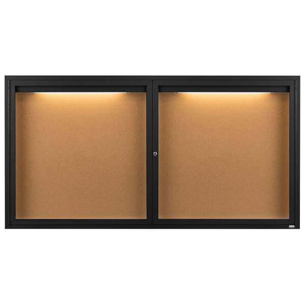 A black Aarco enclosed bulletin board cabinet with lights on.