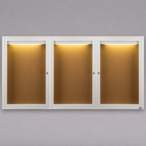 A row of three white Aarco bulletin board cabinets with lights inside.