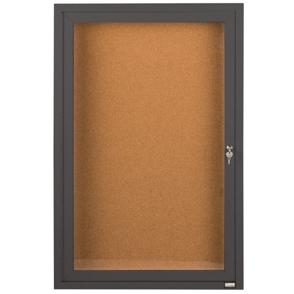 A brown cork bulletin board cabinet with a key-locking black framed door.