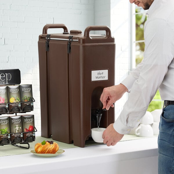 A man pours coffee from a Cambro dark brown beverage dispenser.