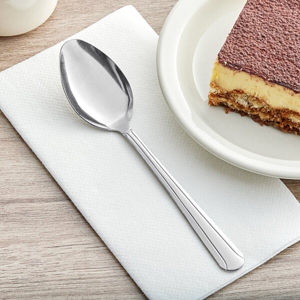 A piece of Choice Dominion stainless steel dinner/dessert spoon next to a piece of cake on a white plate.