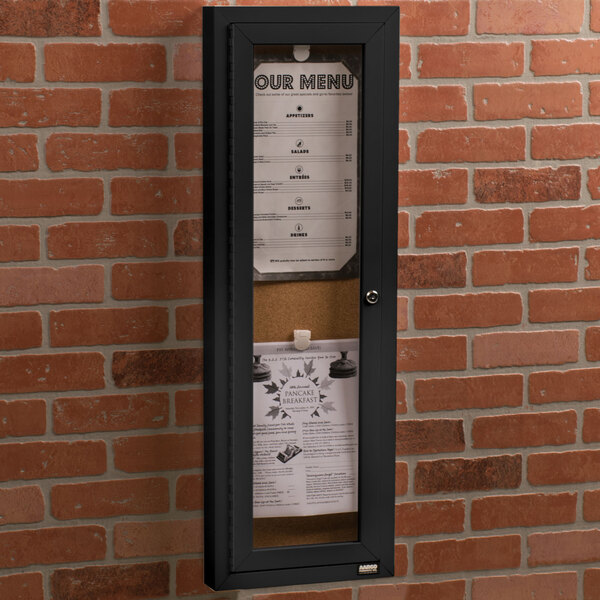 An Aarco black indoor bulletin board with a menu inside a glass door.