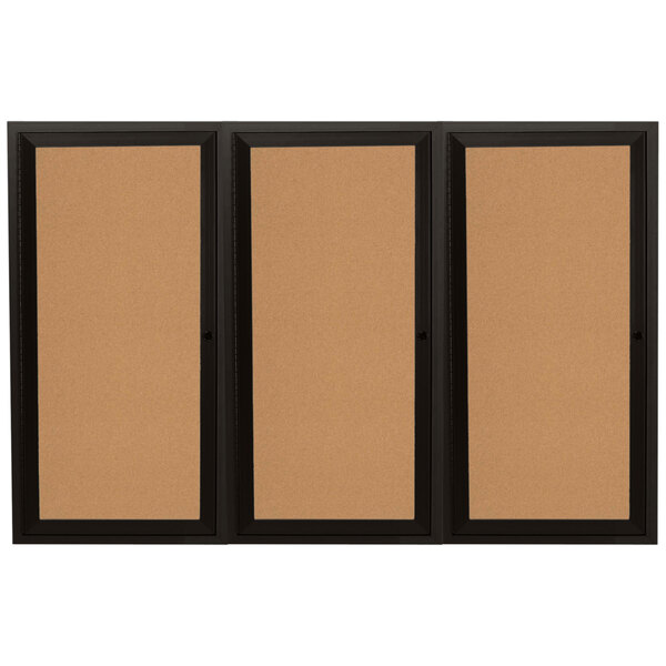 A brown cork board with black frame behind three doors.